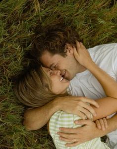 a man and woman laying in the grass hugging each other with their arms around one another