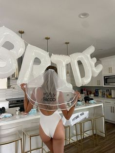 the back of a woman in a white bodysuit holding up balloons that say bride