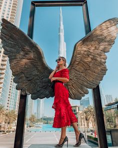 a woman in a red dress standing next to an angel statue with her hands on her hips