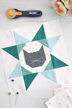 a quilter's block with scissors next to it on a white wooden table