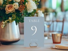 a table number sign sitting on top of a table next to a vase filled with flowers