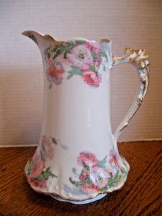 a white and pink flowered pitcher sitting on top of a wooden table next to a wall