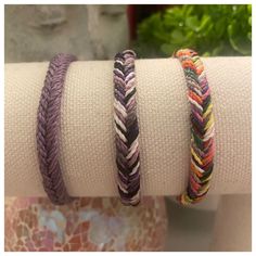 three different colored bracelets on top of each other in front of a potted plant