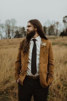 a man with long hair and a beard wearing a suit in the middle of a field