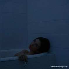 a woman leaning on the edge of a bathtub in the dark with her hand resting on the edge of the tub