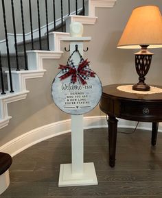 a welcome sign in front of a stair case with a lamp on the end table