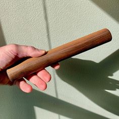 a hand holding a wooden stick in front of a white wall with shadows on it