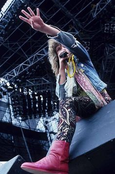 a woman sitting on the edge of a stage with her hands in the air while talking on a cell phone