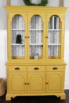 a yellow china cabinet with black and white wallpaper