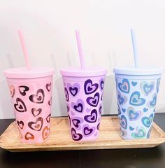 three colorful cups with straws in them on a wooden tray next to a white wall