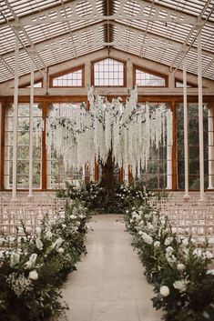 an indoor wedding venue with white flowers and greenery on the aisle, surrounded by windows