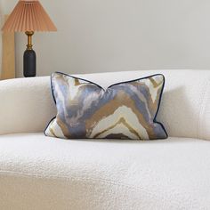 a white couch with a blue and brown pillow on it next to a table lamp