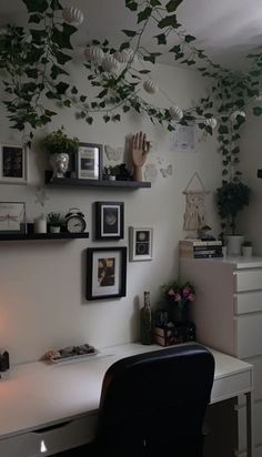 a white desk topped with a computer monitor next to a wall covered in pictures and plants