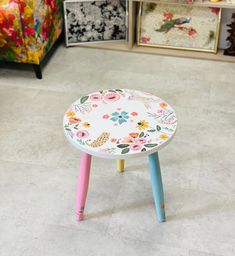 a small stool with flowers painted on it in front of a colorful couch and chair