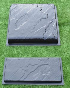 two black stone slabs sitting on top of green grass