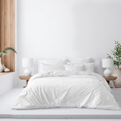 a bed with white linens and pillows in a minimalist bedroom setting, surrounded by potted plants