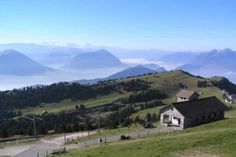 a small house on the side of a hill with mountains in the background and foggy sky