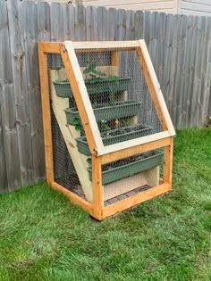 a chicken coop with chickens in it sitting on the grass next to a wooden fence