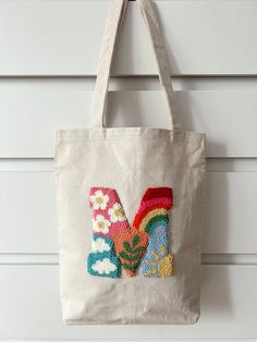 a tote bag with the letter m in sequins on it hanging from a hook