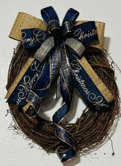 a blue and gold christmas wreath hanging on a white wall with ribbon around the front