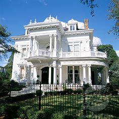 a large white house sitting on top of a lush green field next to a fence