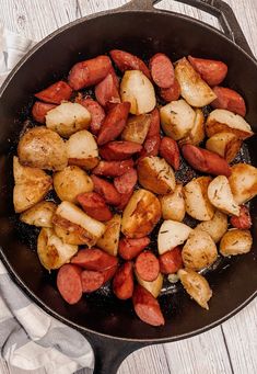 cooked sausage and potatoes in a skillet on a white wooden table with napkins