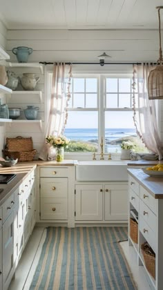 a kitchen with an open window and striped rug in front of the countertop, along with white cabinets