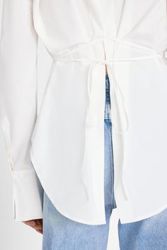 This luxurious Frame blouse is crafted from organic cotton poplin in a crisp Blanc hue. Its modern design features a subtle slit in the back and slim wrap ties, allowing you to accentuate your waist or remain breezy by tying loose. This stylish garment is sure to make a statement. 100% Organic Cotton Machine Wash Cold 28.5" Long From Shoulder MODEL IS 5'10.5" TALL/178.5CM AND IS WEARING A US SIZE S Bow Back Shirt, Classic White Blouse, Tie Waist Shirt, Tie Shirt, Simple Tees, Tie Blouse, Military Inspired, Poplin Shirt, Frame Denim