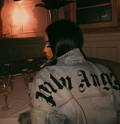 a woman wearing a jean jacket sitting at a table with wine glasses in front of her