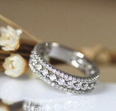 two wedding rings sitting next to each other on top of a white surface with flowers in the background