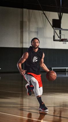 a man holding a basketball on top of a gym floor in front of a hoop