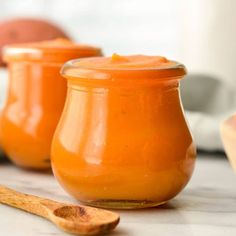 three small jars filled with orange colored liquid and wooden spoons next to each other