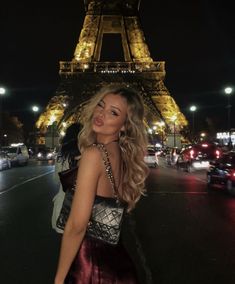 a woman standing in front of the eiffel tower at night with her hand on her hip