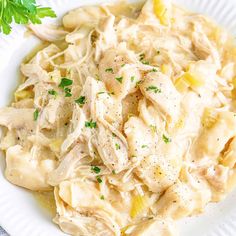 a white plate topped with pasta covered in chicken and parsley next to a green leafy garnish