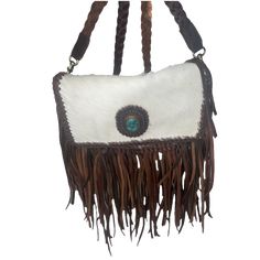 Style number: ADBGM272C. Brown leather bag. Black & white cowhide. Leather braid strap & edges. Leather fringe coming out of braided edge. Turquoise stone on front. 2 inside pockets. 1 zipper pocket on back. Adjustable strap. Button closure. 100% genuine full grain leather. White Bohemian Leather Bags, Bohemian White Leather Bags, Cowhide Purse, Brown Leather Bag, Braided Strap, Leather Fringe, Braided Leather, Turquoise Stone, Full Grain Leather