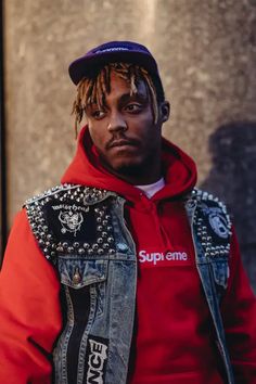 a man with dreadlocks wearing a red hoodie and denim jacket standing in front of a building