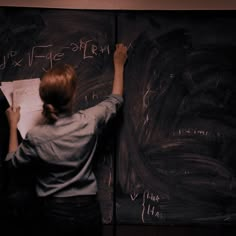 a woman writing on a blackboard with chalk