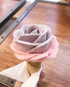 someone is holding an ice cream cone with pink and grey frosting on it,