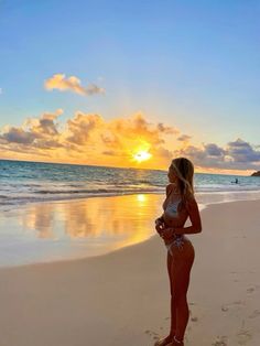 a woman standing on top of a sandy beach next to the ocean at sunset or dawn