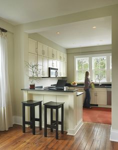 a woman standing in a kitchen next to two stools