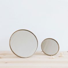 two round mirrors sitting on top of a wooden table next to a white flower vase