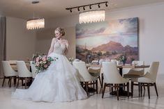 a woman standing in front of a dining room table with flowers on it and a painting behind her