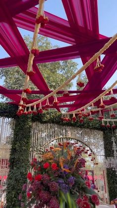 an outdoor wedding venue decorated with pink and red flowers, greenery and hanging decorations