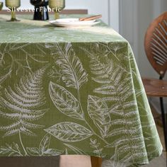 a green table cloth with white leaves on it and two wine bottles in the background