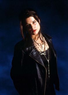 a woman wearing a black leather jacket and chain necklace standing in front of a dark blue sky