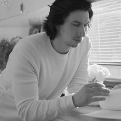 a man sitting at a table with a book in front of him and looking down