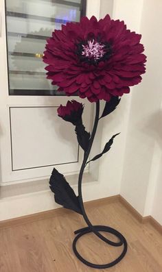 a large purple flower sitting on top of a wooden floor next to a white door