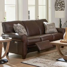 a living room with brown leather furniture and wood flooring, windows in the background