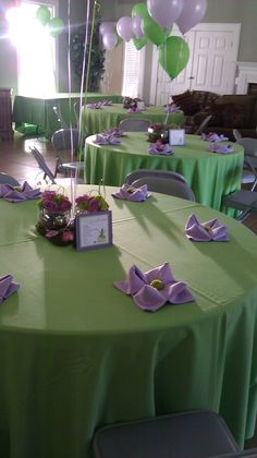 a green table topped with lots of purple and white flowers next to balloons in the air