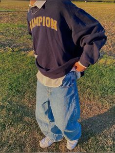 a young boy standing in the grass with his hands on his hips wearing a champion sweatshirt